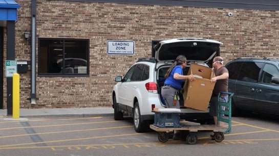 Two people loading a box into the back of a white SUV.