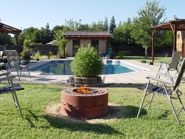 Concrete tree ring fire pit next to lawn chairs and a pool.