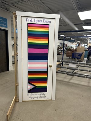 A door painted with a Pride flag, the words Pride Opens Doors, and a quote.