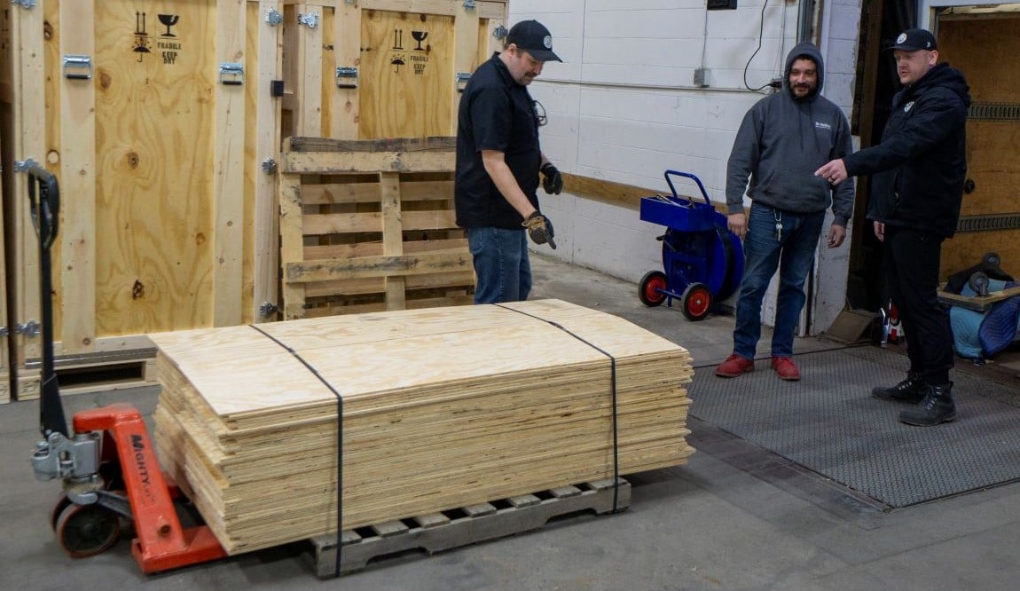 A pallet of plywood and three warehouse workers.