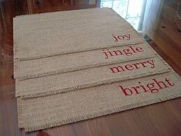 Burlap place mats that say "Joy, jingle, merry," and "bright."