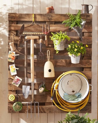 Pallet hanging on a wall and holding garden tools.