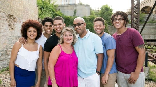 A large smiling Habitat family by a stone bridge.