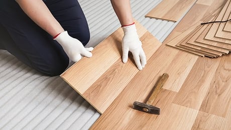 Close-up of a person's hands installing vinyl plank flooring.