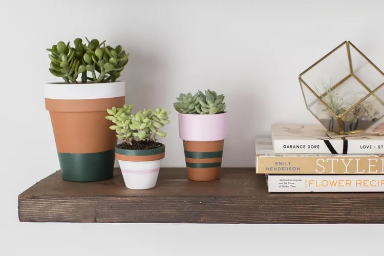 Three striped flower pots on a shelf next to some books.