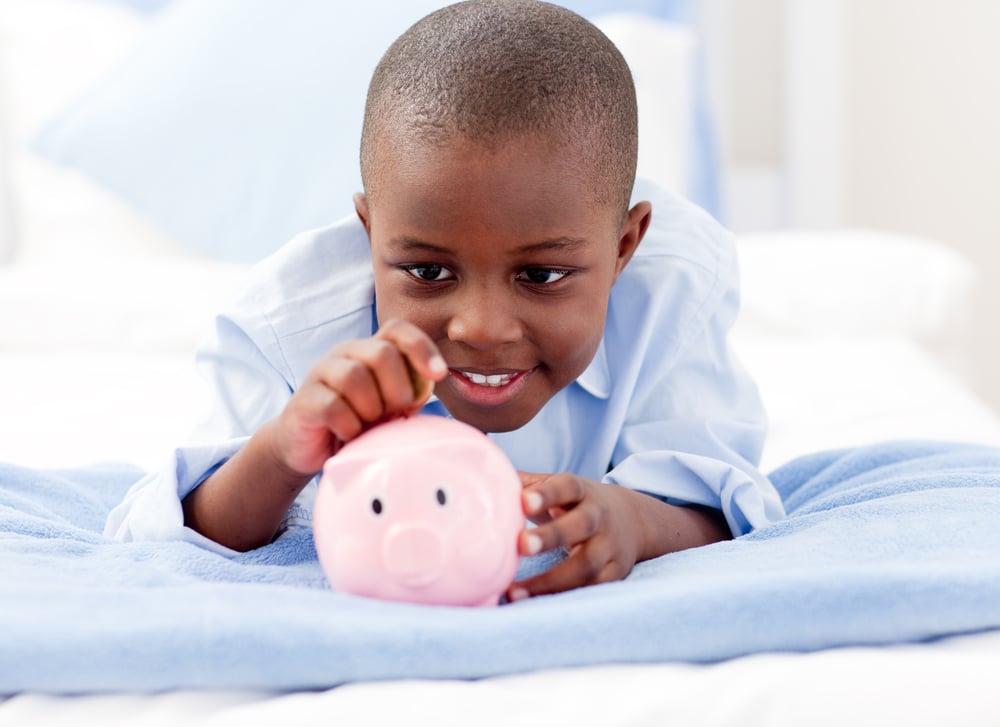 Young Boy lying on his bed putting money into a piggy bank