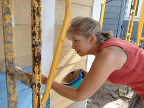 A woman leaning over to paint siding.