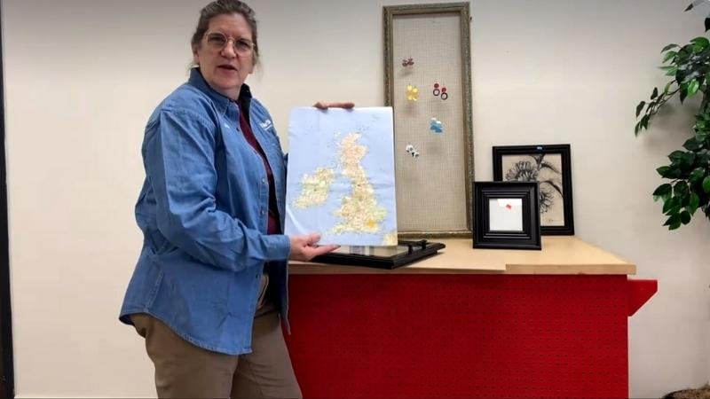 Jan holding a picture of the UK in front of picture frames.