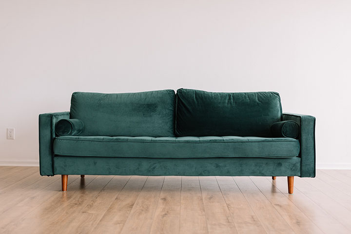 Green couch in an empty room with hardwood floors and a white wall.