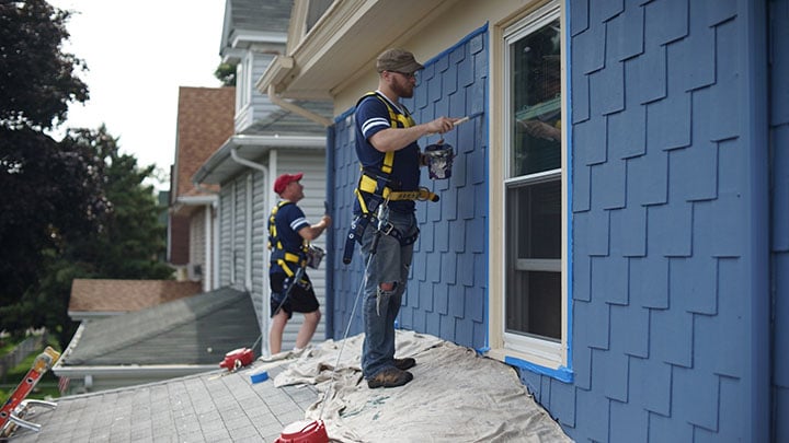 Two painters painting blue siding.