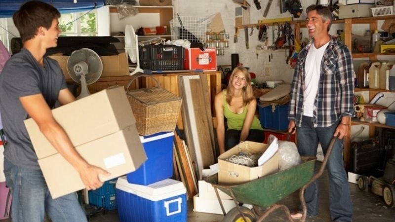 A parent and teen children sorting through boxes and items in their garage.