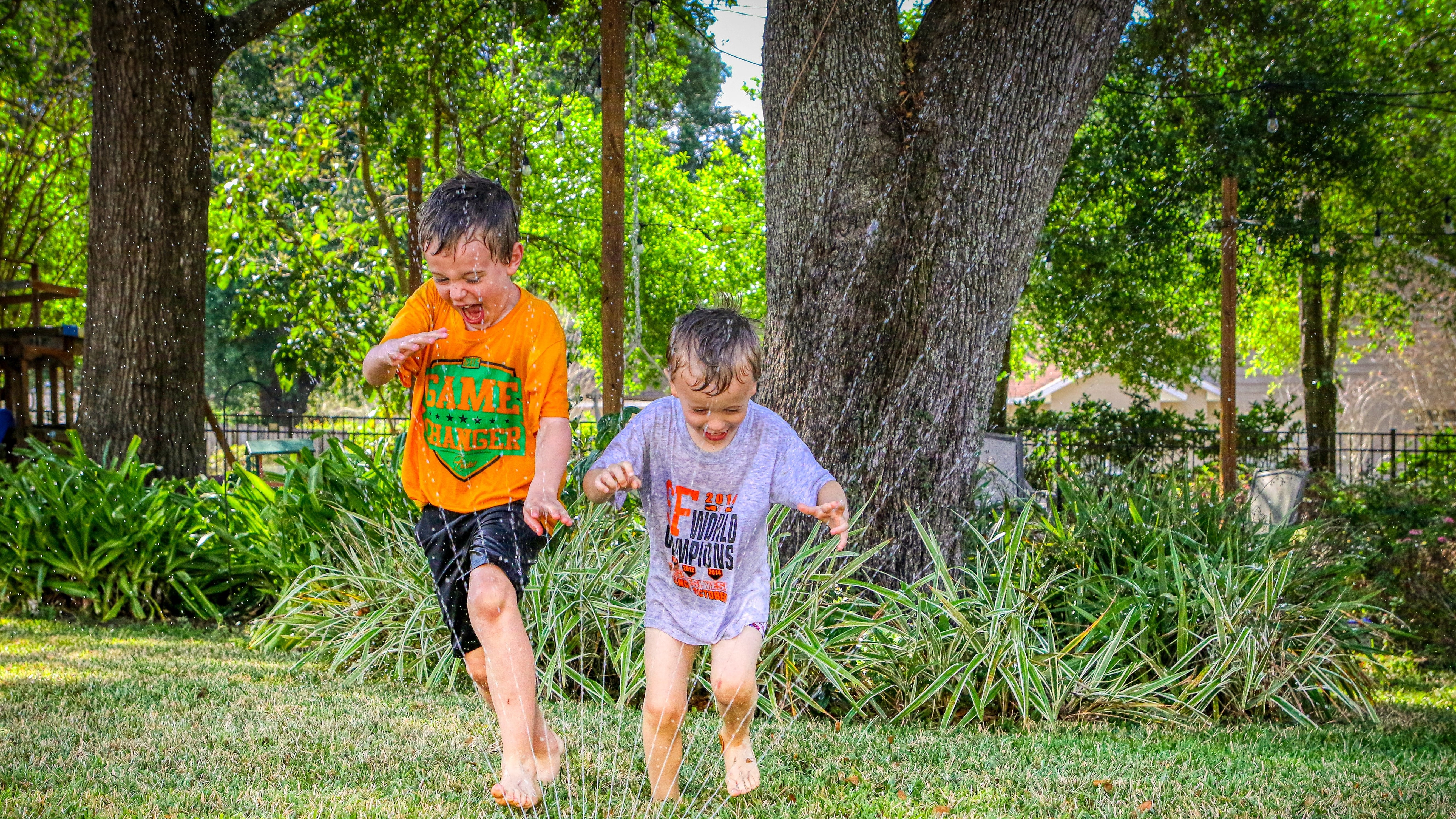 Two kids running through a sprinkler.